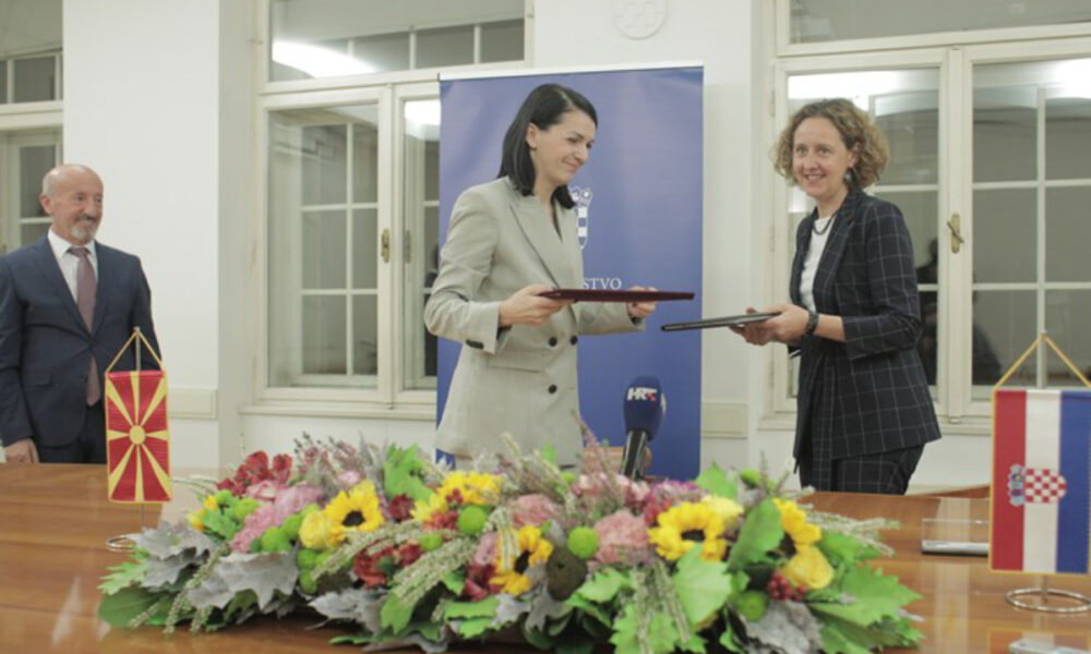 Ova slika prikazuje diplomatski događaj između Makedonije i Hrvatske. Slika prikazuje dvoje ljudi, vjerojatno predstavnika dviju država, kako razmjenjuju dokumente za bijelim stolom. Stol ima cvjetni aranžman i zastavice obiju država. Pozadina ima plavi natpis s bijelim tekstom.