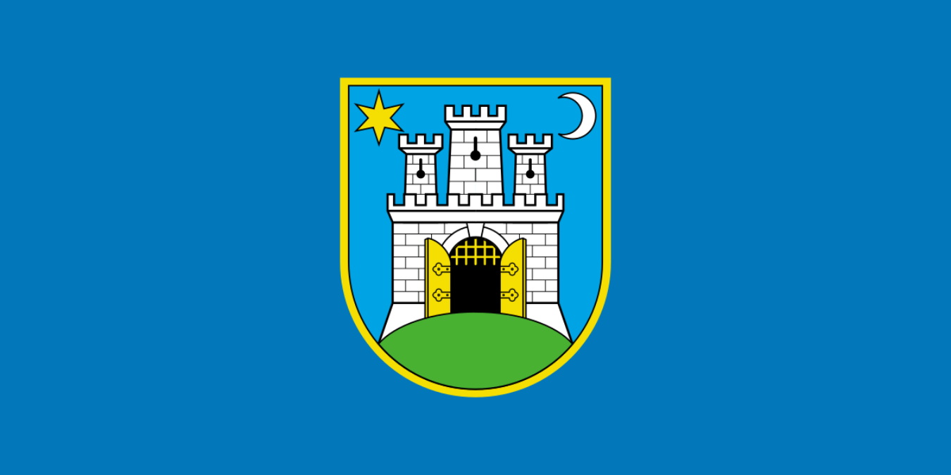 Slika prikazuje grb na plavoj pozadini. Grb sadrži prikaz bijelog dvorca s crnim konturama i zlatnim vratima, postavljenog na zelenom terenu. Iznad dvorca je jedna zvijezda i mjesec.