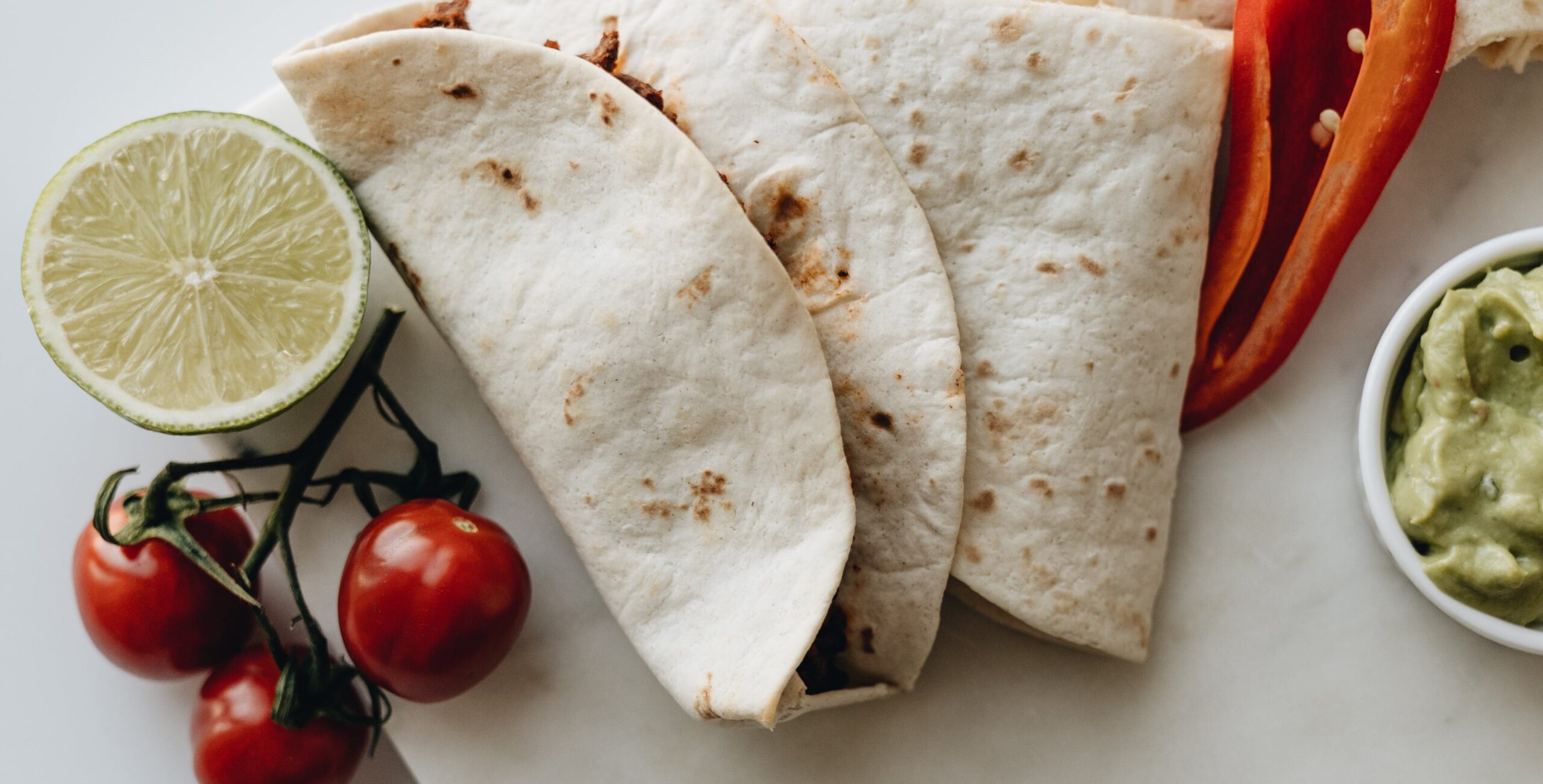 Ovo je fotorealistična slika tri mekana taco na bijelom tanjuru. Tako su presavijeni i imaju punjenje koje izgleda kao povrće Tanjur također ima narezanu crvenu papriku, klinčić limuna i malu zdjelicu guacamole. Na tanjuru se nalaze i nekoliko trešanja rajčice na vinu.