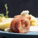 Na slici je poslužen tanjur s ukusnim obrokom. Vidljiv je komad mesa omotan slaninom, popraćen pire krumpirom.
