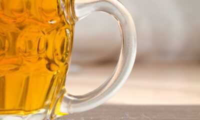 Slika prikazuje krupni plan čaše piva. Pivo je zlatne boje. Pozadina je zamagljena, ali čini se da je drvena površina, usmjeravajući pažnju na čašu.
