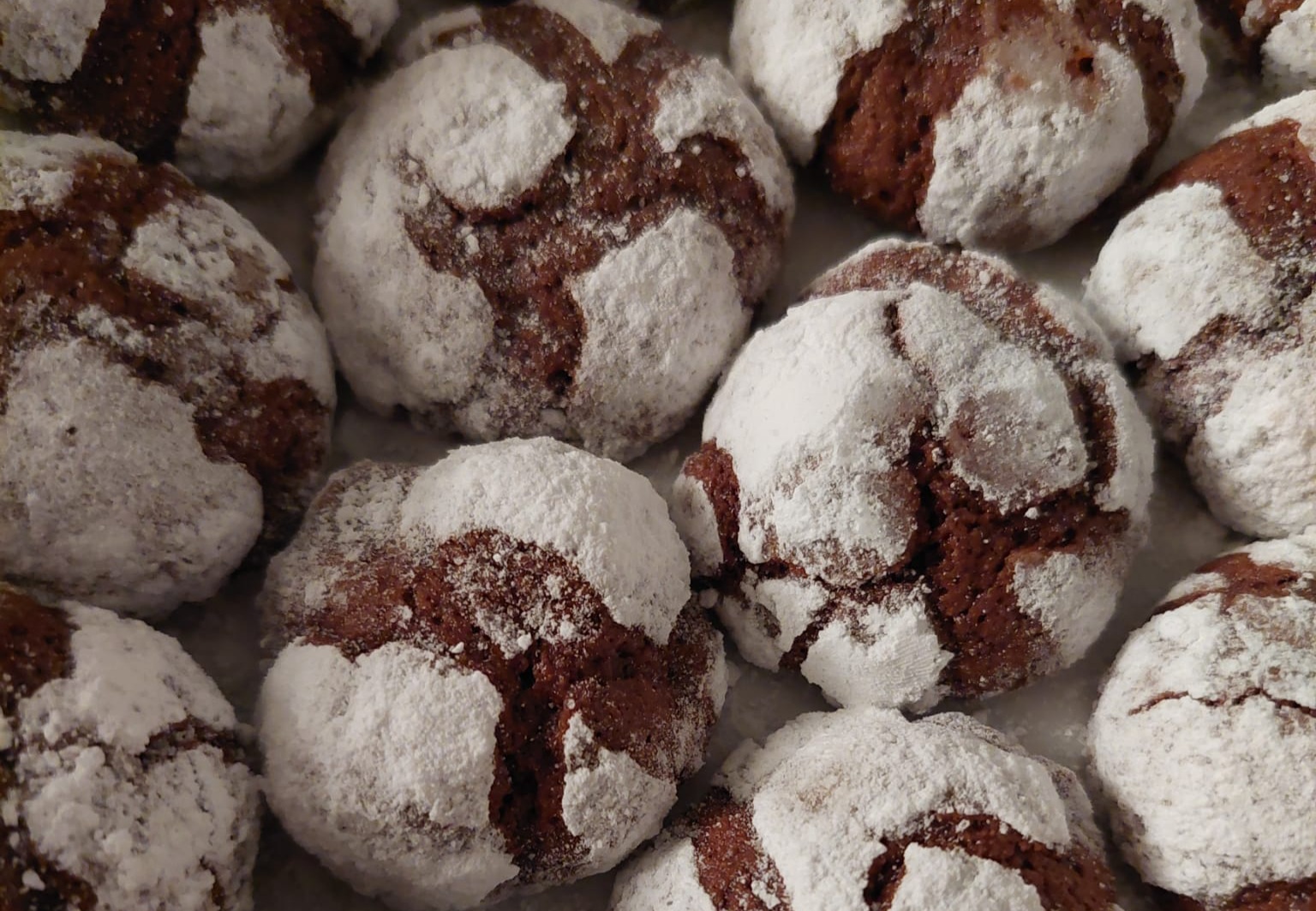 Ova slika prikazuje skupinu čokoladnih kolačića posutih šećerom u prahu. Kolačići su smeđi s bijelim šećerom koji se drži za pukotine na površini, stvarajući kontrastnu i apetitnu sliku.