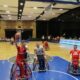 Na slici je košarkaška utakmica u kojoj igrači koriste invalidska kolica. Igrač u crvenoj opremi s natpisom “CROATIA” pokušava postići koš, dok ga igrač u plavoj opremi pokušava blokirati. Pozadina prikazuje košarkaški teren i tribine.