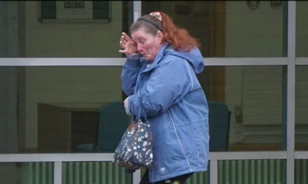 Fotografija prikazuje ženu koja briše suze, ima na sebi traper jaknu i kosu zavezanu u rep. Djeluje kao da je izašla iz zgrade.