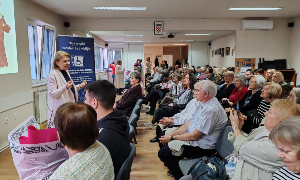 Ova slika prikazuje skupinu ljudi u prostoriji koji slušaju prezentaciju.