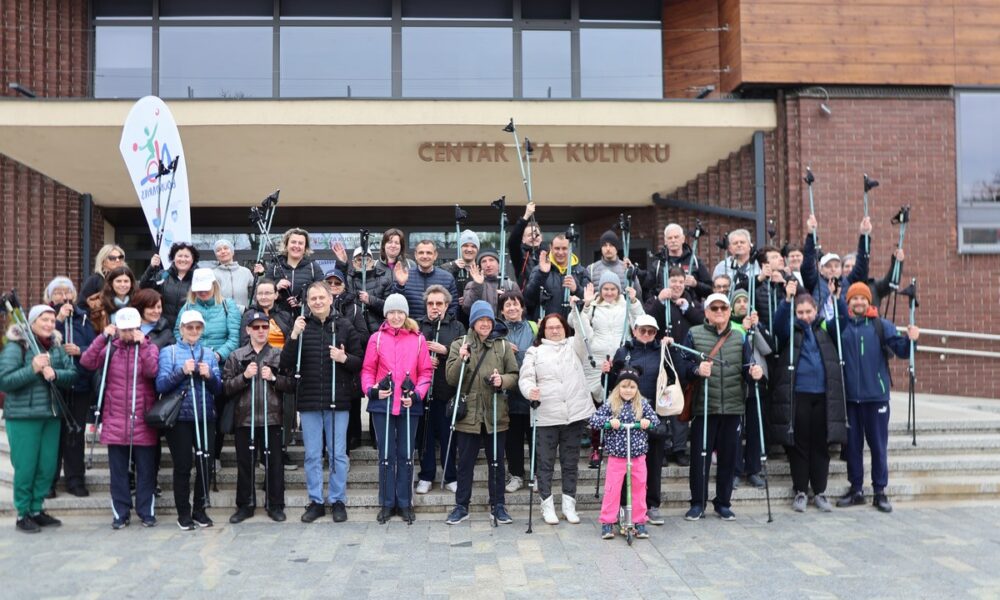 Fotografija prikazuje grupu ljudi koji drže štapove za hodanje ispred zgrade s natpisom 'CENTAR ZA KULTURU'. Grupa se sastoji od osoba različitih dobnih skupina, uključujući djecu i odrasle. Zgrada je modernog dizajna s velikim staklenim prozorima i vratima. Na lijevoj strani slike nalazi se zastava ili transparent s nečitkim tekstom zbog kuta i udaljenosti.