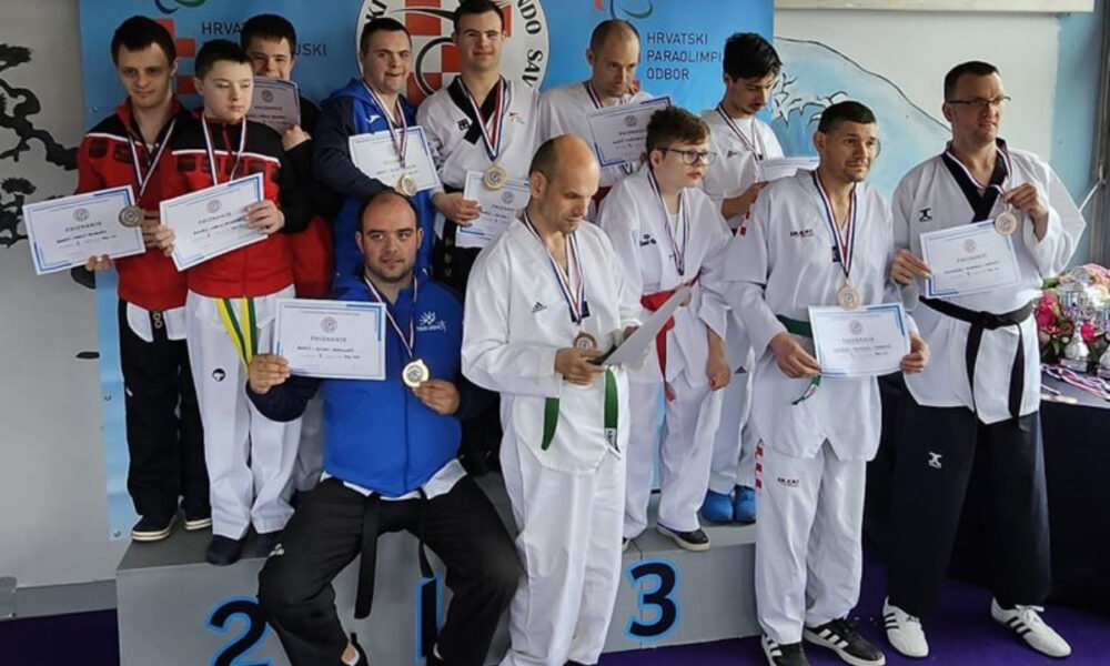 Na slici je grupa ljudi koji su osvojili nagrade na natjecanju u parataekwondou. svi drže diplome u rukama. Pozadina prikazuje plakat sa natpisom “PARA TAEKWONDO” Na podiju su označena mjesta 1, 2 i 3, što ukazuje na pobjedničke pozicije.