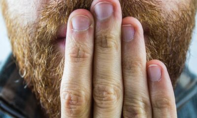 Fotografija prikazuje osobu koja pokriva dio lica rukom. Na slici se vidi crvena brada i ruka s prstima koji prekrivaju usta i nos.