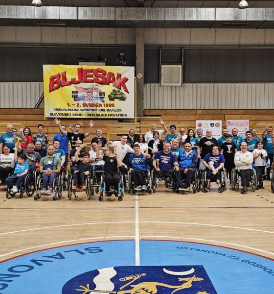 Na slici su igrači u invalidskim kolcima u sportskoj dvorani. Vjerojatno na nekom sportskom natjecanju. Iza njih je žuti plakat na kojem crvenim slovima piše 'BLJESAK'. Parket je smeđe boje, a vidi se i centar igrališta koji je obojan u plavo.