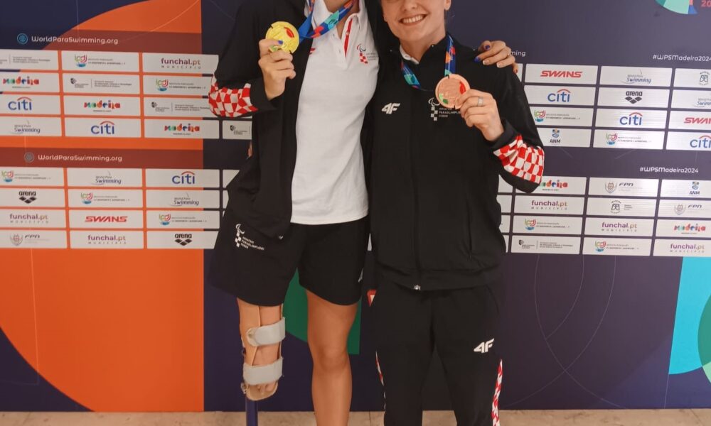 Na slici su dvije osobe sa zlatnom i brončanom medaljom što upućuje na to da su osvojile prvo i treće mjesto na natjecanju. Jedna osoba ima protezu. Osoba sa brončanom medaljom nosi trenirku na kockice. Iza njih je natpis Madeira 2024. paraswiming.