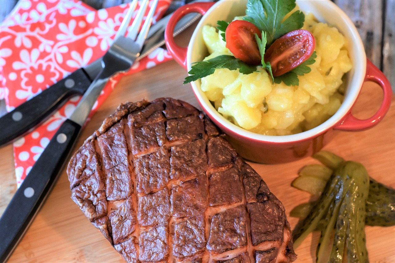 Na fotografiji je pečeni steak poslužen na drvenoj ploči. Uz steak se nalazi nož i vilica postavljeni na crvenu i bijelu tkaninu s cvjetnim uzorkom. Pored toga, tu je i zdjela sa salatom od krumpira ukrašena peršinom i prepolovljenim cherry rajčicama, te nekoliko kiselih krastavaca. Ambijent sugerira da je obrok pripremljen kod kuće.