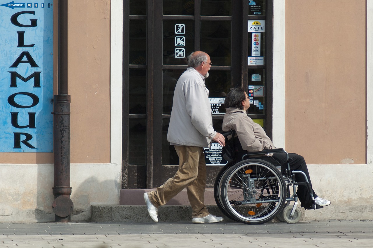 Na slici se nalaze dvije osobe; jedna hoda, a druga je u invalidskim kolicima. Prolaze pokraj trgovine s staklenim vratima na kojima se nalaze razne naljepnice. S lijeve strane slike vidljiv je veliki plavi znak s natpisom “GLAMOUR”. Zgrada ima klasičan arhitektonski dizajn s bež zidovima i smeđim obrubom oko prozora i vrata. Uz pločnik stoji metalna ulična svjetiljka obojana u crno.