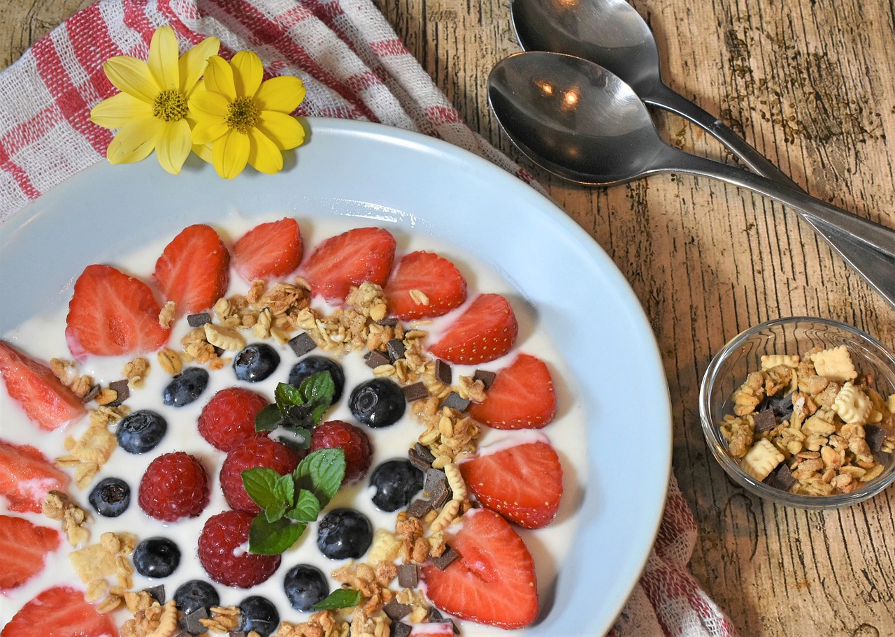 Na fotografiji je zdjelica s jogurtom, raznim svježim voćem po kojem su posipani orašasti plodovi. Sve sugerira zdravi doručak i otvara apetit.