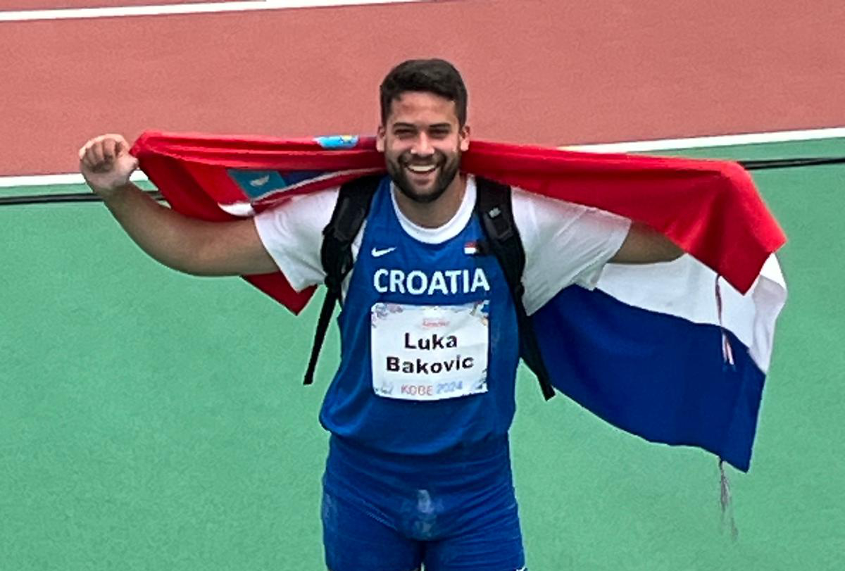 Na slici je osoba koja nosi sportsku opremu s natpisom “Croatia” i ime “Luka Baković”. Osoba drži hrvatsku zastavu raširenu iza sebe.