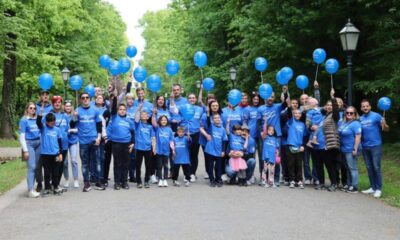Fotografija prikazuje mnoštvo članova Udruge Osmijeh. Odjeveni su u plave majice i drže plave balone. Nalaze se na otvorenom, u parku.