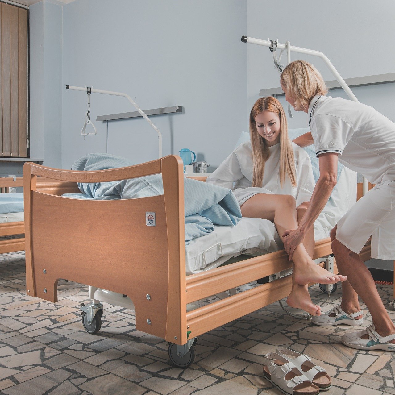 Slika prikazuje mediinsku sestru koja pomaže pacijentici ustati iz bolničkog kreveta.