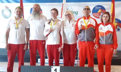 Na slici je grupa od šest osoba koje stoje na pobjedničkom postolju. Svi nose sportske uniforme i medalje oko vrata. Troje osoba s lijeve strane su u bijelim uniformama, a troje s desne strane u crvenim. U pozadini se vide zastave i transparent na kojem piše “LAS GABIAS SHOOTING CENTER - SPAIN”. Radi se o natjecanju u streljaštvu, što se može zaključiti po tekstu napisanom na transparentu.