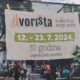 Na slici je plakat za događaj "Dvorišta" koji se održava od 12. do 23. srpnja 2024. godine. Plakat obilježava desetu godišnjicu zagrebačkih dvorišta s natpisom "Svako ima svoju priču." U pozadini plakata je fotografija ljudi koji sjede u dvorištu, uživajući u društvu i opuštenoj atmosferi. Donji dio plakata sadrži logotipe organizatora i kontakte na društvenim mrežama, kao i web stranicu dvorišta.in.