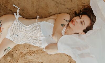 Fotografija prikazuje mlađu ženu koja leži na pijesku u bijelom jednodjelnom kupaćem kostimu