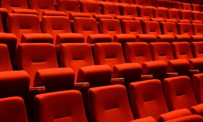 Na slici se nalazi unutrašnjost prazne kinodvorane ili kazališta s redovima crvenih sjedala. Sjedala su presvučena crvenim baršunastim materijalom i uredno su poredana u nekoliko redova, stvarajući dojam simetrije i reda. Rasvjeta je prigušena, fokusirajući se na sjedala.
