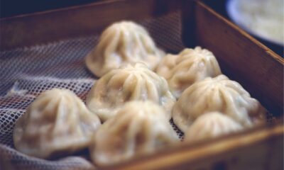 Fotografija prikazuje nekoliko kineskih knedli, poznatih kao dim sum, posluženih u bambusovoj pari. Knedle su bijele boje s naborima na vrhu i izgledaju kao da su upravo skuhane ili pripremljene za posluživanje. Pozadina je zamagljena, što naglašava knedle u prvom planu. Fotografija bi mogla biti zanimljiva zbog detalja i teksture knedli koje sugeriraju svježinu i ukusnost jela, a također može biti relevantna za teme povezane s kineskom kuhinjom ili gastronomijom općenito.