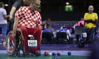 Na slici se nalazi paraboćar u majici s crveno bijelim kockicama što znači da je hrvatski sportaš. Na zelenoj podlozi nalaze se jedna bijela, te više plavih i crvenih boći. Na kolicima u kojima se boćar nalazi stavljena je i tabla na kojoj piše sponzor 'TOYOTA', crveno slovo C ime i zemlja sportaša.