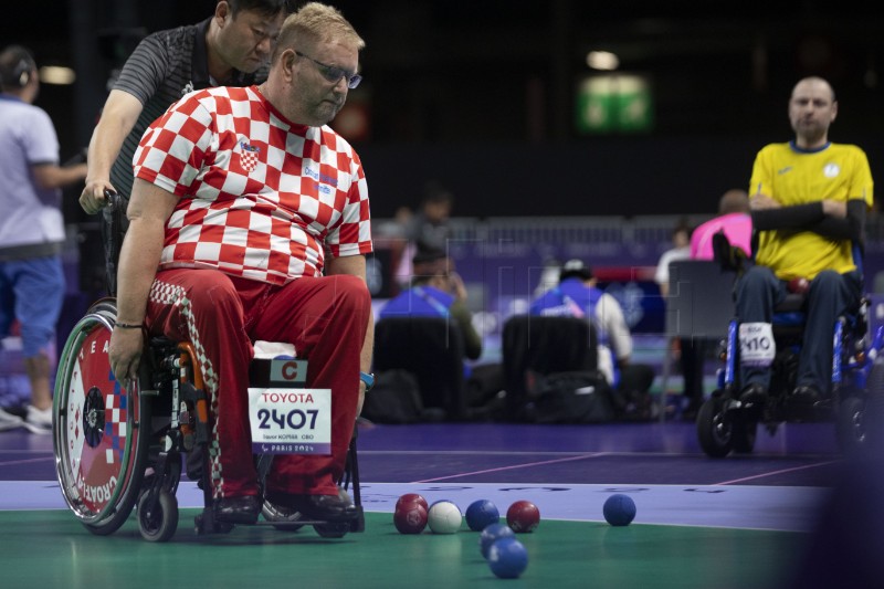 Na slici se nalazi paraboćar u majici s crveno bijelim kockicama što znači da je hrvatski sportaš. Na zelenoj podlozi nalaze se jedna bijela, te više plavih i crvenih boći. Na kolicima u kojima se boćar nalazi stavljena je i tabla na kojoj piše sponzor 'TOYOTA', crveno slovo C ime i zemlja sportaša.