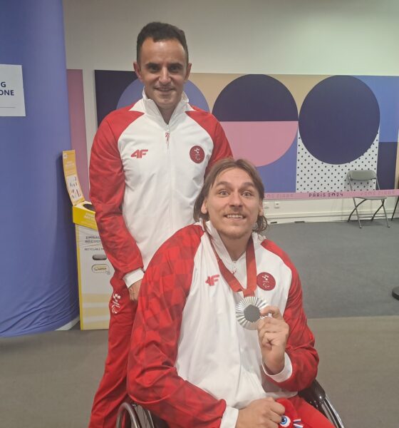 Na slici su dvije osobe u sportskoj odjeći, jedna od njih u invalidskim kolicima. Oboje nose bijele jakne s crvenim rukavima, s grbom i logom "4F". Osoba u kolicima drži srebrnu medalju, ponosno je pokazuje prema kameri i smiješi se. Iza njih je natpis "NO FILMING IN MIXED ZONE", a u pozadini se nalazi šaren zid s motivima Pariških Paraolimpijskih igara 2024.