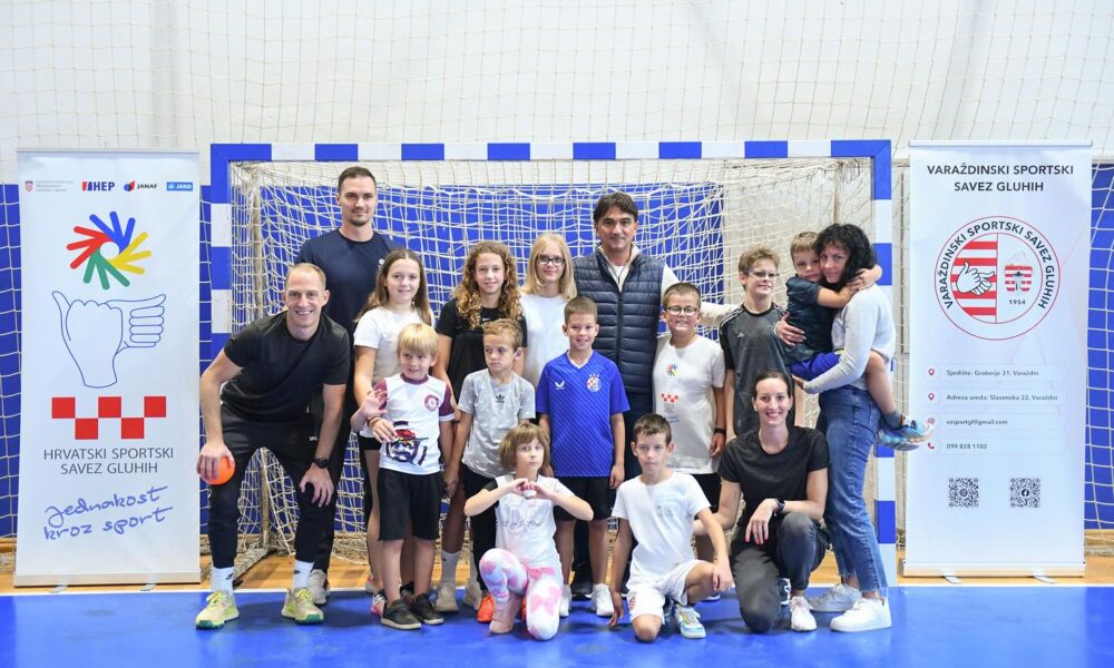 Fotografija prikazuje izbornika Hrvatske s djecom i roditeljima kako poziraju za sliku u golu na terenu u sportskoj dvorani. S obje strane gola stoje baneri. Na jednom piše 'Hrvatski sportski savez gluhih' nacrtan je znak i piše ime sponzora 'HEP', dok na drugom piše 'Varaždinski sportski savez gluhih'. po sredini njega je također nacrtan znak, a navedene su i ostale informacije poput adrese, maila i broja telefona saveza.