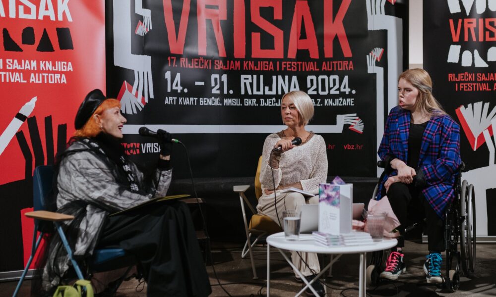 Fotografija prikazuje predstavljanje knjige poezije Branke Kostić. Četiri osobe sjede ispred pozadine s velikim plakatima na kojima piše “VRISAK” i informacije o 17. Riječkom sajmu knjiga i festivalu autora koji se održava od 14. do 21. rujna 2024. godine.