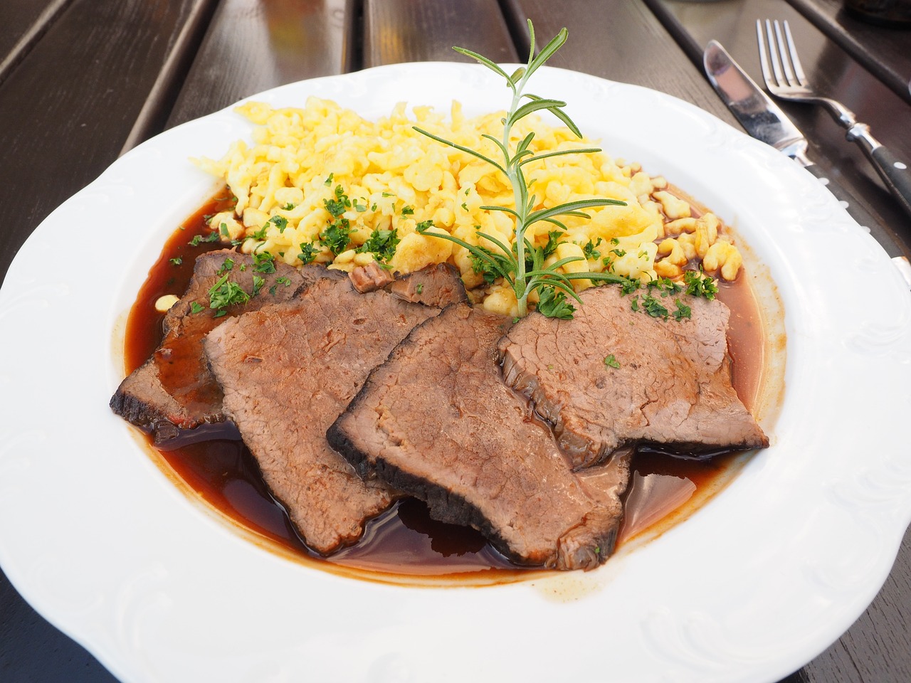 Na fotografiji je prikazan tanjur s hranom koji sadrži tri kriške pečenog mesa, vjerojatno govedine, prelivenog umakom. Uz meso se nalazi prilog od spaetzle, vrste njemačkih knedli ili tjestenine. Jelo je ukrašeno grančicom ružmarina i posipano sitno sjeckanim peršinom.