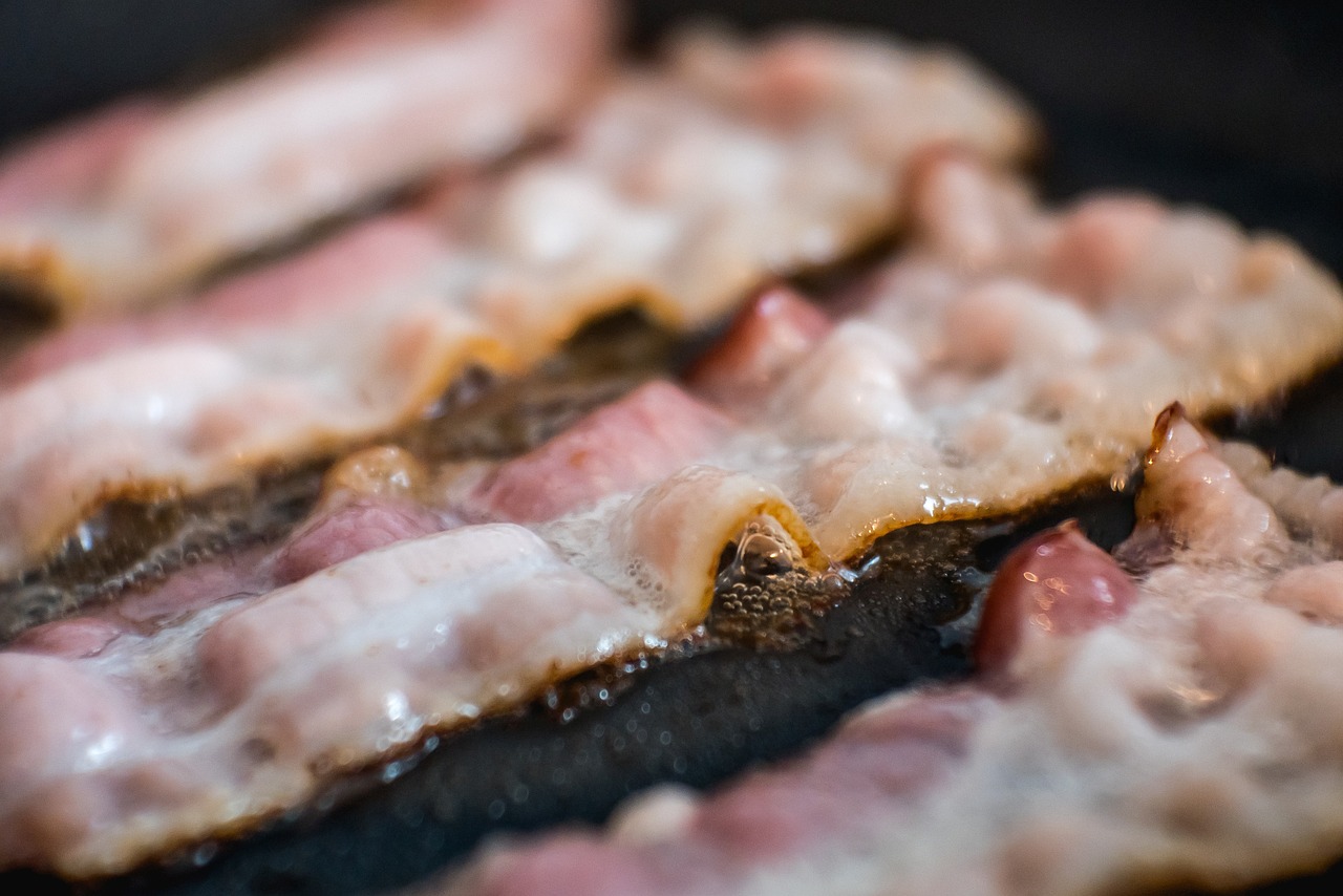 Na fotografiji je prikazano nekoliko komada slanine koji se peku na tavi. Slanina je u različitim fazama pečenja, s nekim dijelovima koji izgledaju hrskavo i tamnije, dok su drugi još uvijek svjetliji i manje ispečeni. Površina tave je crna, što ukazuje na to da bi mogla biti od lijevanog željeza ili sličnog materijala. Ova fotografija može biti zanimljiva zbog prikaza procesa kuhanja, posebno za one koji uživaju u gastronomiji ili traže vizualni prikaz pripreme hrane.