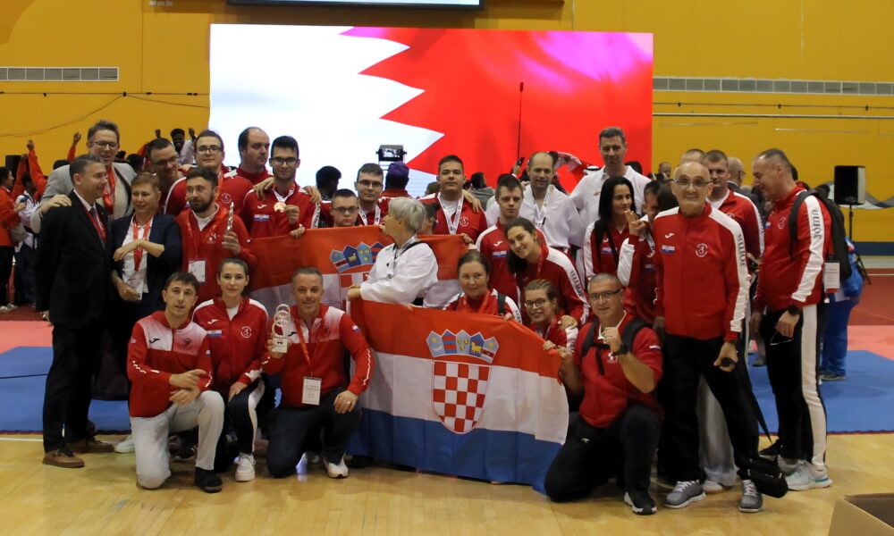 Fotografija prikazuje više ljudi, većina ih je u crvenim trenirkama, a neki su i u kimonima. Ispred sebe razvili su hrvatsku zastavu što znači da je riječ o Hrvatima. Neki od ljudi oko vrata imaju medalje, što znači da je riječ o nekom natjecanju. Iza ljudi je plava strunjača i video zid koji je obojan pola u bijelo, a pola u crveno te predstavlja Bahreinsku zastavu.