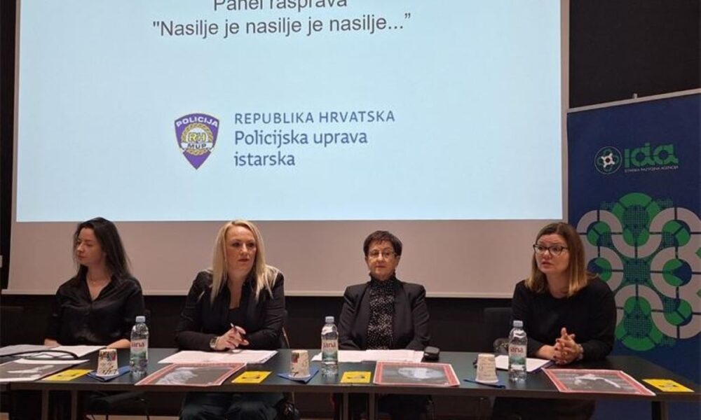 Fotografija prikazuje panel raspravu pod nazivom "Nasilje je nasilje je nasilje..." koju organizira Policijska uprava istarska, Republika Hrvatska. Na slici se vidi četiri osobe koje sjede za stolom, ispred njih su boce vode, šalice i papiri. Iza njih je projekcija s nazivom rasprave i logotipom policije.