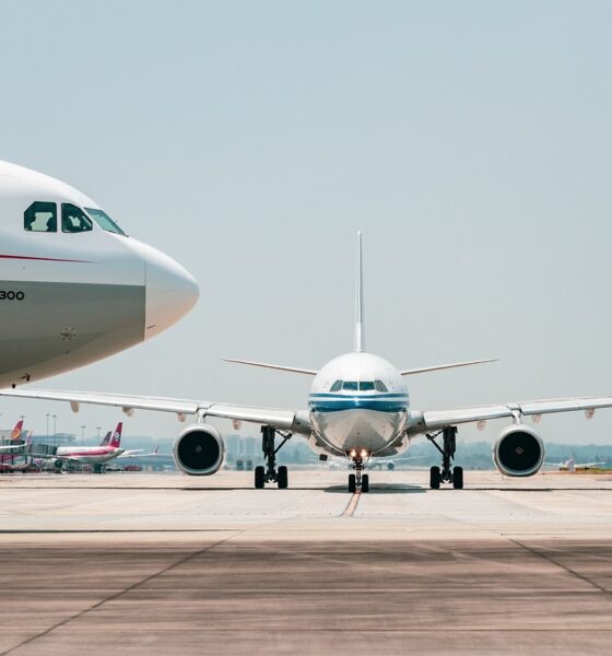 Dva aviona stoje na pisti aerodroma, jedan u prvom planu sa natpisom "Airbus A330-300" na trupu, dok je drugi u pozadini. Na pisti su i drugi avioni u daljini pod vedrim nebom.