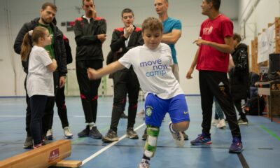 Fotografija prikazuje nekoliko ljudi, a između ostalog jednog dječaka sa protezom na jednoj nozi koji pokušava šutnuti nešto.