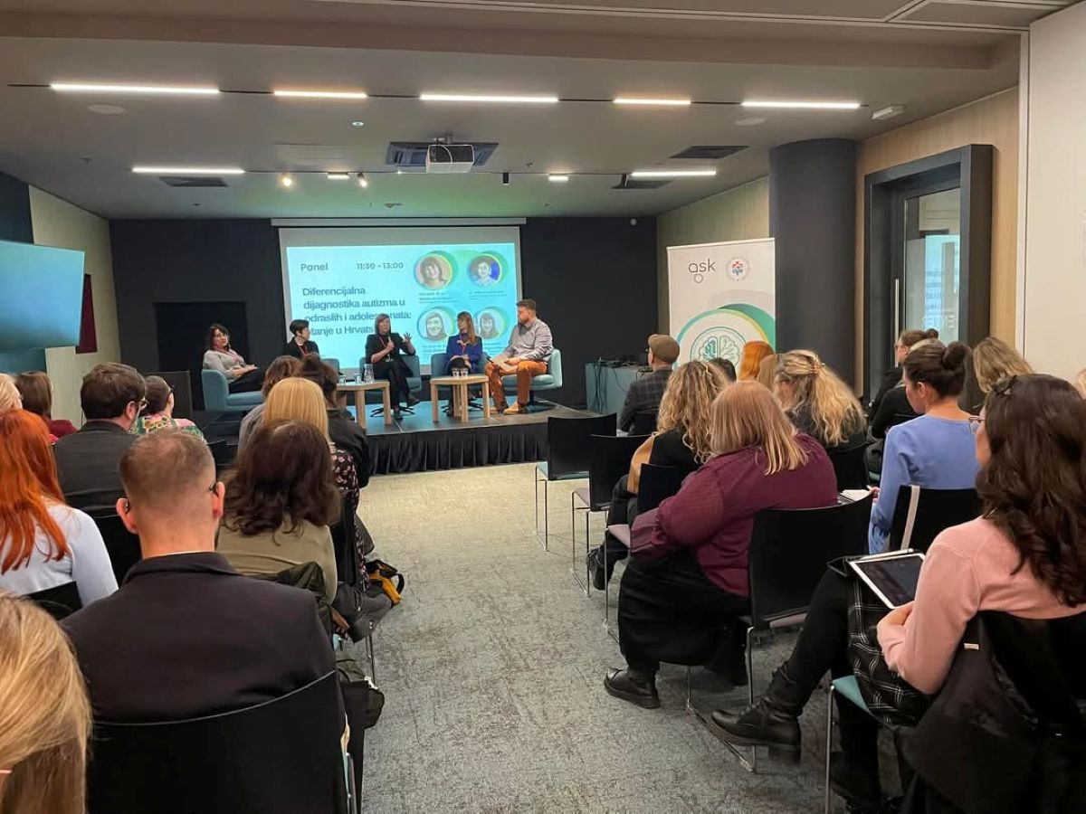 Fotografija prikazuje panel diskusiju na temu „Diferencijalna dijagnostika autizma u odraslih i adolescenata: stanje u Hrvatskoj“. Panel se održava u konferencijskoj sali pred mnogobrojnom publikom. Na pozornici su četiri panelista koji sudjeluju u raspravi, a iza njih je projektor s prikazom informacija o panelu i slikama sudionika. U publici se nalaze ljudi različitih dobnih skupina, a neki od njih drže bilježnice ili tablete. S desne strane slike vidljiv je banner s logotipom organizacije „ask“.
