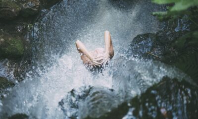Na fotografiji se vidi osoba koja stoji ispod vodopada, dok voda pada na nju. Podigla je ruke i stavila ih na glavu, dok je okružena stijenama prekrivenim mahovinom i zelenilom. Prizor djeluje osvježavajuće i odražava ljepotu prirode, naglašavajući sklad između čovjeka i okruženja. Fotografija odiše osjećajem slobode i povezanosti s prirodom.
