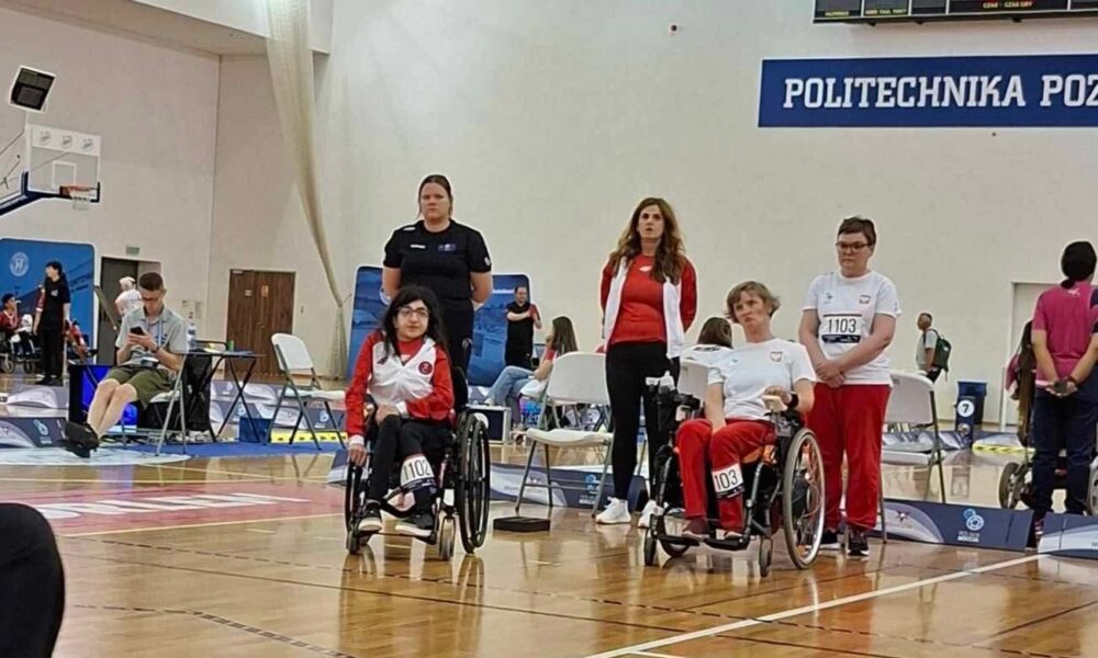 Fotografija prikazuje poćare s invaliditetom kakoo boćaju. Na parketu se vide plave, crvene i jedna bijela boća.