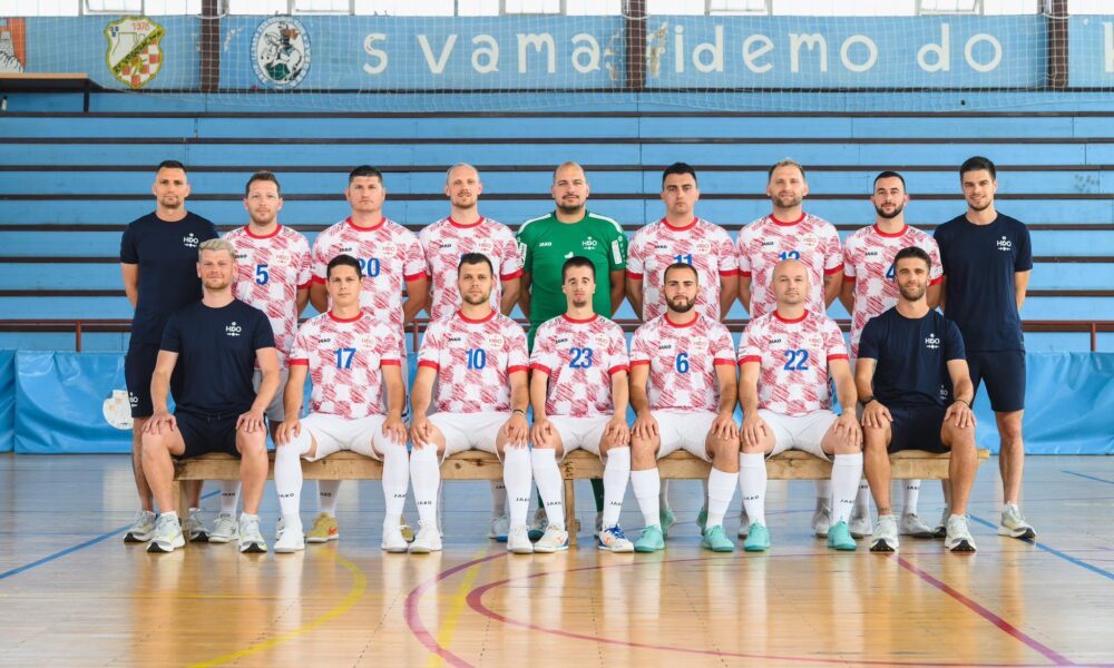 Slika prikazuje tim igrača u crveno-bijelim majicama kako sjede na klupi.