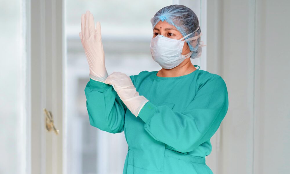 Fotografija prikazuje doktoricu u operacijskoj odjeći kako navlači rukavicu.