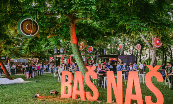 Posjetitelji na otvorenom festivalu Baš Naš, okruženi zelenilom, štandovima i festivalskim dekoracijama.