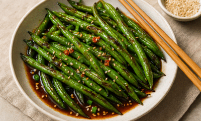 Fotografija prikazuje hrskave mahune pripremljene na azijski način, s tamnim umakom, tostiranim sezamom, čili papričicama i mladim lukom, sve servirano u elegantnoj keramičkoj zdjeli uz štapiće za jelo.