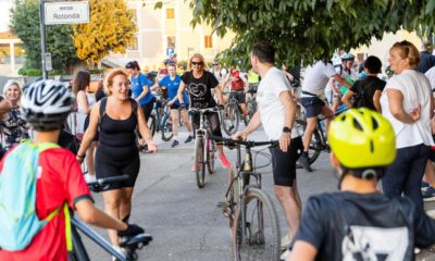 Fotografija prikazuje više ljudi na biciklima te neke ljude koji stoje.