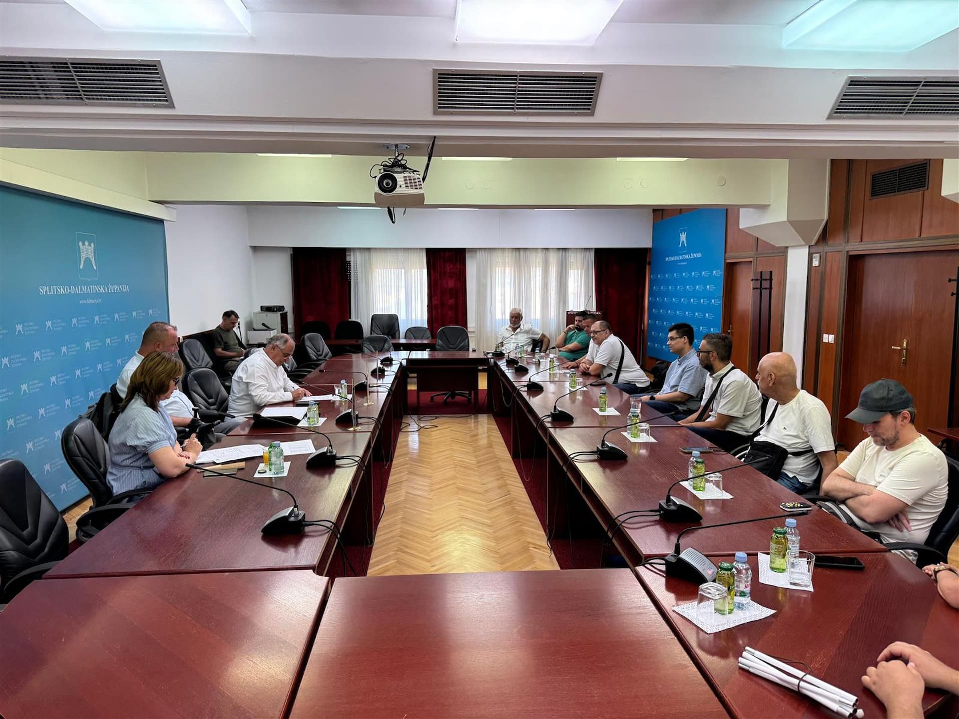 Fotografija prikazuje više ljudi koji sjede za stolom na sastanku.