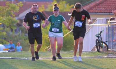 Fotografija prikazuje troje trkača kako prelaze liniju cilja držeći se za ruke, Jedno od to troje trkača ima Down sindrom.