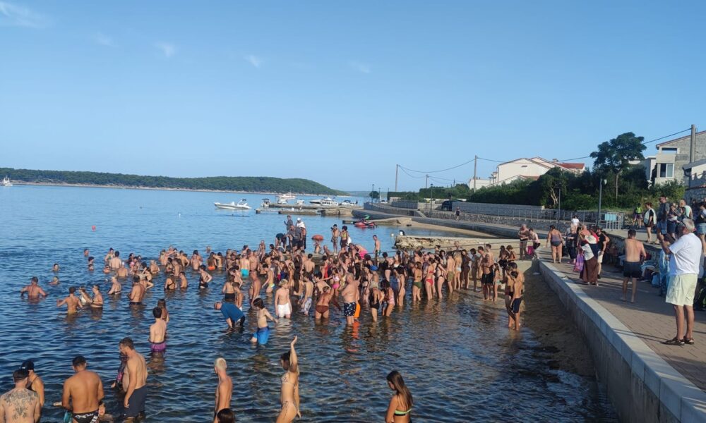 Fotografija prikazuje više ljudi kako se kupa u moru.