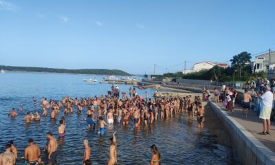 Fotografija prikazuje više ljudi kako se kupa u moru.