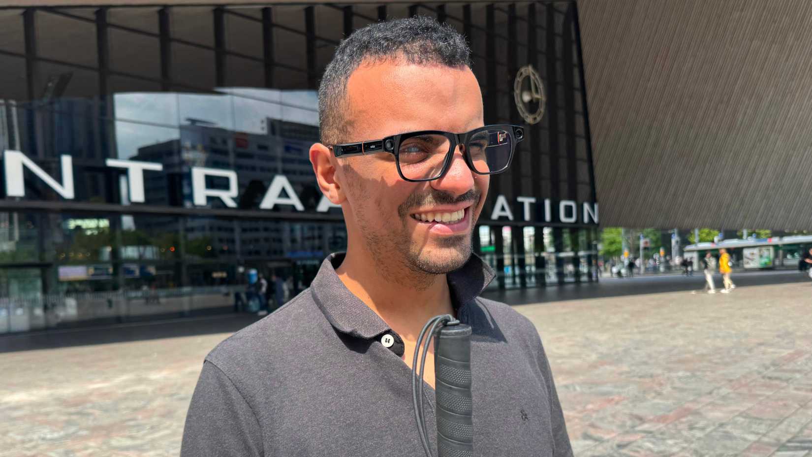 Mladić kratke kose i brade stoji nasmiješen ispred velike zgrade željezničkog kolodvora. Nosi tamne naočale i tamnosivu majicu s ovratnikom, a u ruci drži bijeli štap za slijepe i slabovidne osobe. Iza njega se vidi natpis "CENTRAL STATION" i gradska pozadina.