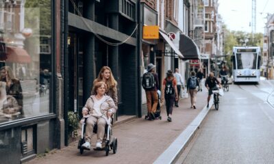 Fotografija prikazuje jednu mlađu ženu kako gura stariju ženu u kolicima. One šetaju po vani i prolaze pokraj nekog izloga.